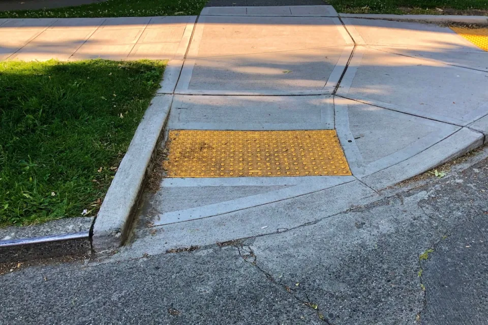 Curb cut at corner of sidewalk with yellow panel with bumps to indicate wheelchair ramp.